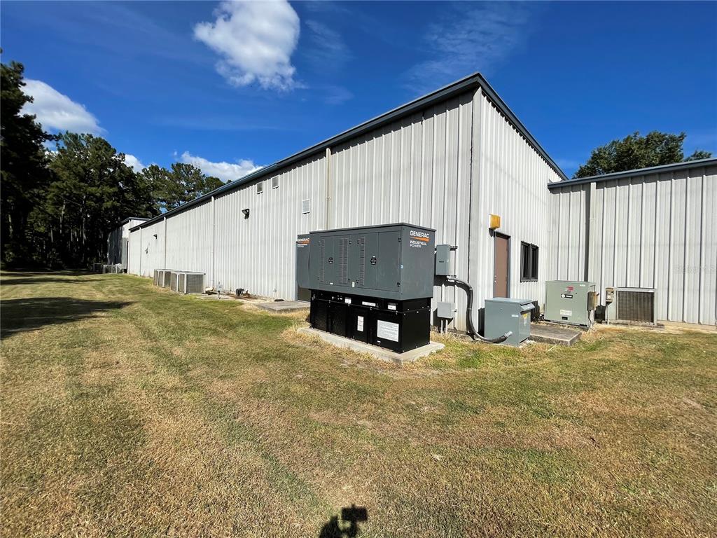 The exterior of a metal industrial building features a large Generac backup generator — 3600 SW 47TH AVENUE, GAINESVILLE, FL