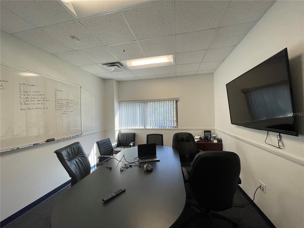 A conference room features a long black table, office chairs, a whiteboard, and a wall-mounted television — 3600 SW 47TH AVENUE, GAINESVILLE, FL