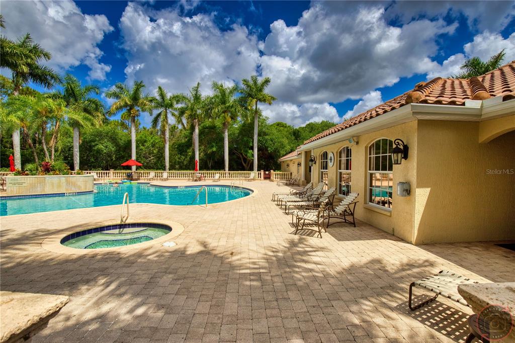 A swimming pool and hot tub sit on a paved patio beside a residential building — 4528 CANCELLO GRANDE AVENUE, VENICE, FL
