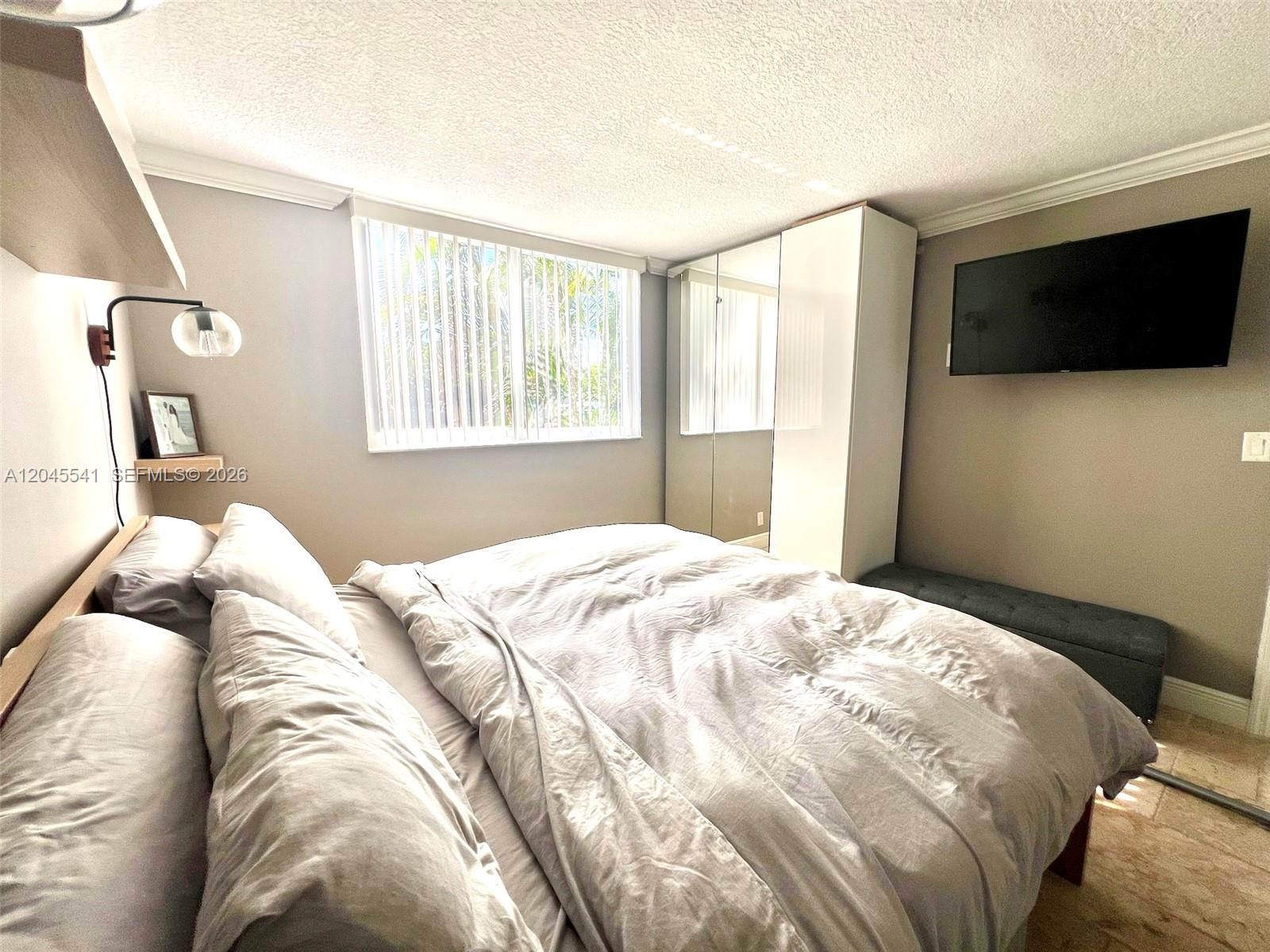 A bedroom features a bed, a wall-mounted television, a white wardrobe, and a window — 689 NE 6th Ct # 1080, Boynton Beach FL 33435, BOYNTON BEACH, FL