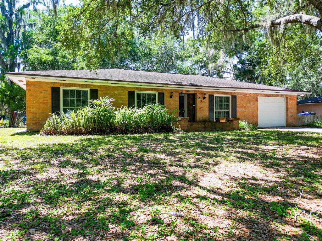 A single-story brick house with a white garage door and large trees in the yard — 18202 OAKDALE RD, ODESSA, FL