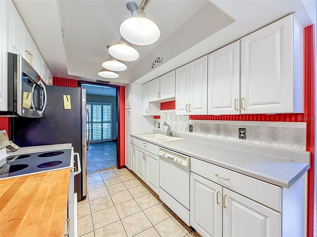 A galley kitchen features white cabinets, a light countertop, stainless steel appliances, and red walls — 18202 OAKDALE RD, ODESSA, FL