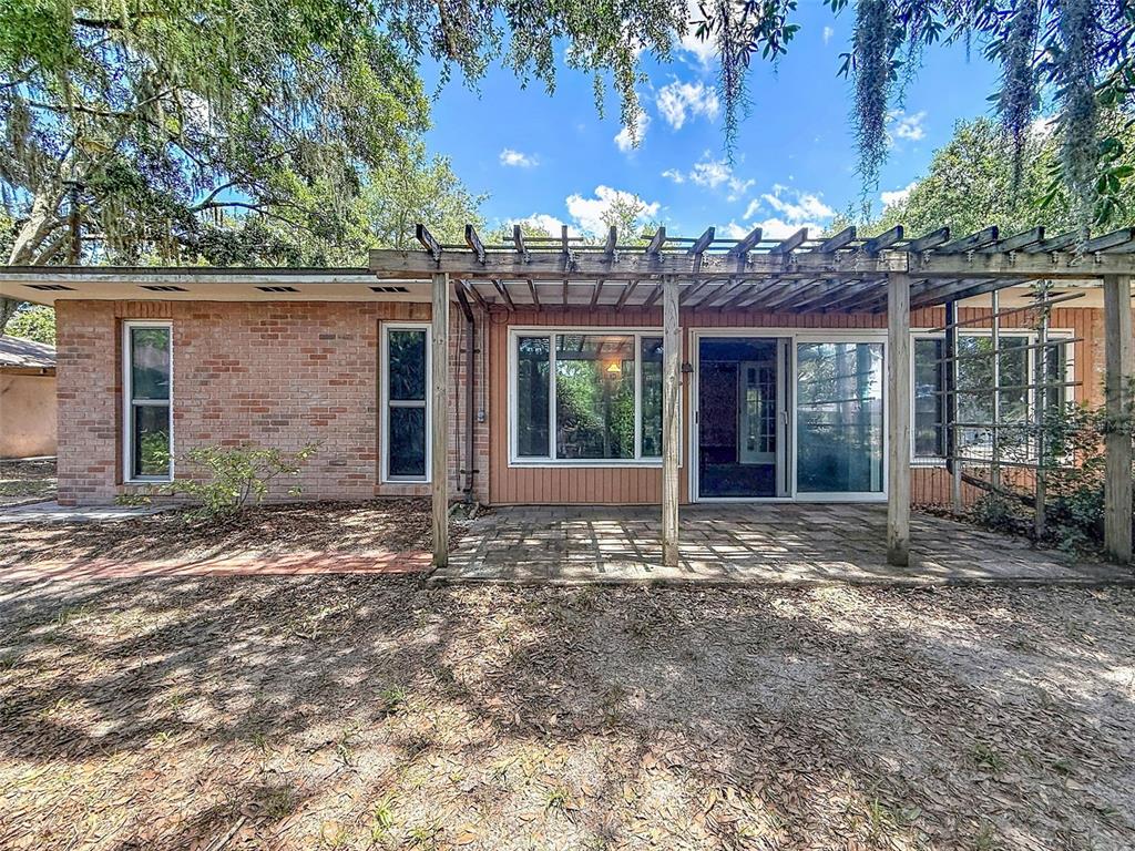A brick house exterior features a patio covered by a wooden pergola and sliding doors — 18202 OAKDALE RD, ODESSA, FL