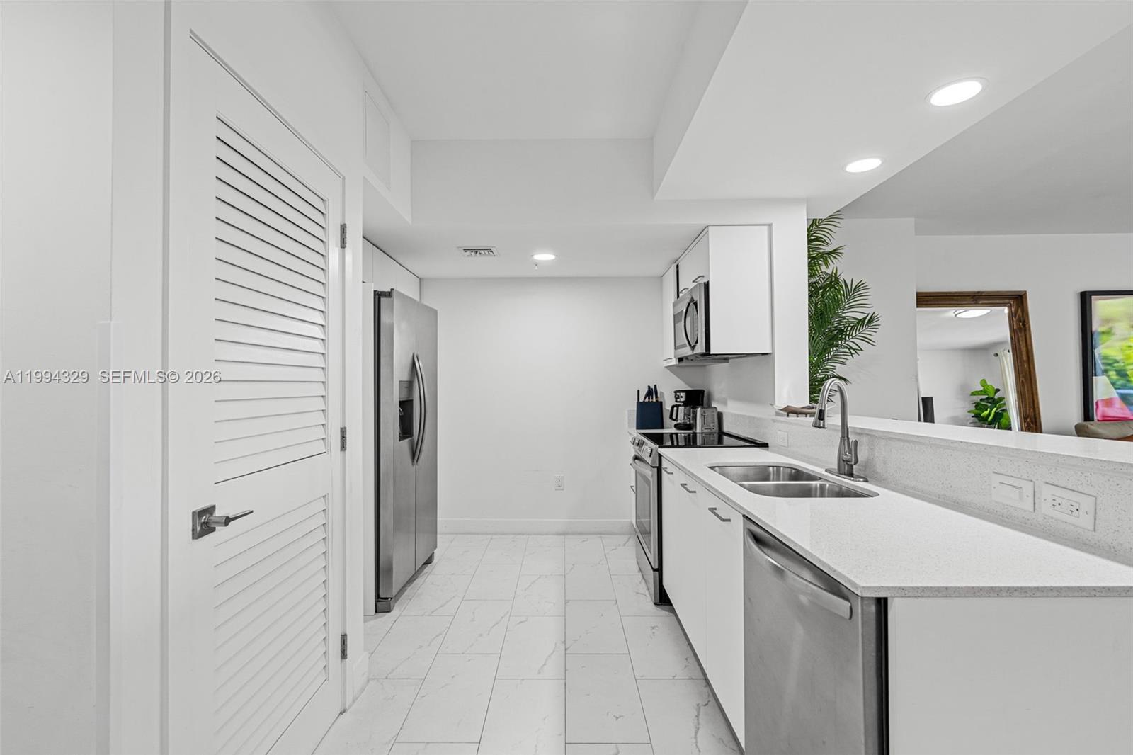 A modern kitchen features white cabinets, stainless steel appliances, and white marble-look tile flooring — 1850 Monroe St # 310, Hollywood FL 33020, HOLLYWOOD, FL