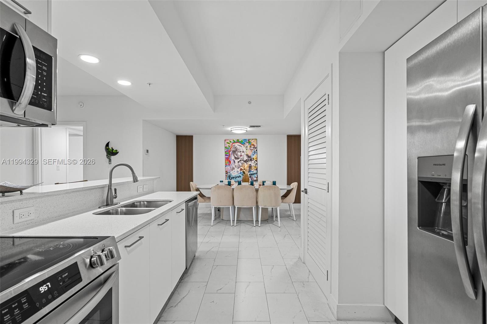 A modern kitchen with white cabinetry and stainless steel appliances opens to a dining area — 1850 Monroe St # 310, Hollywood FL 33020, HOLLYWOOD, FL
