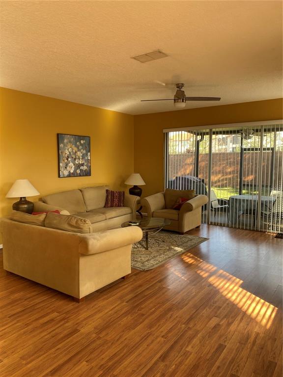A living room with yellow walls, tan furniture, wood-look flooring, and a sliding glass door — 2632 GALLIANO CIRCLE, WINTER PARK, FL