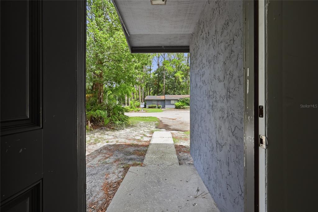 A view from an open doorway looking out onto a concrete walkway and wooded area — 5929 NW 23 TERRACE, GAINESVILLE, FL