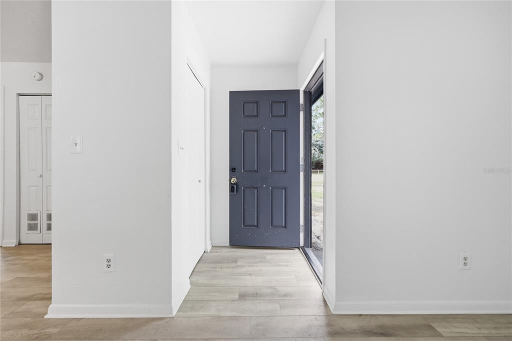 An entryway features light wood-look flooring, white walls, and a dark gray six-panel front door — 5929 NW 23 TERRACE, GAINESVILLE, FL