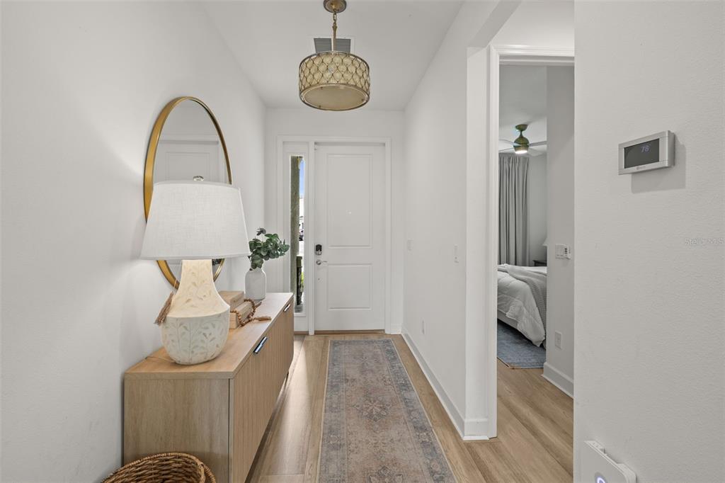 A bright entryway features a wooden console table, a patterned runner, and a modern light fixture — 3541 GREAT BANYAN WAY, WESLEY CHAPEL, FL