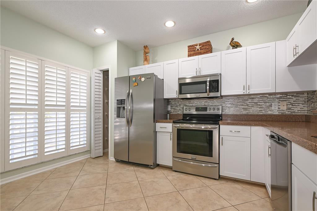 A kitchen with white cabinets, stainless steel appliances, granite countertops, and tile flooring — 11300 HARBOR WAY UNIT 1731, LARGO, FL