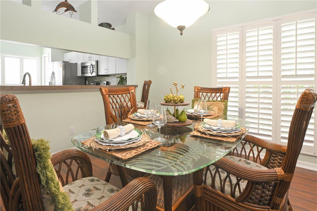 A dining room features a glass-topped table with wicker chairs and plantation shutters — 11300 HARBOR WAY UNIT 1731, LARGO, FL