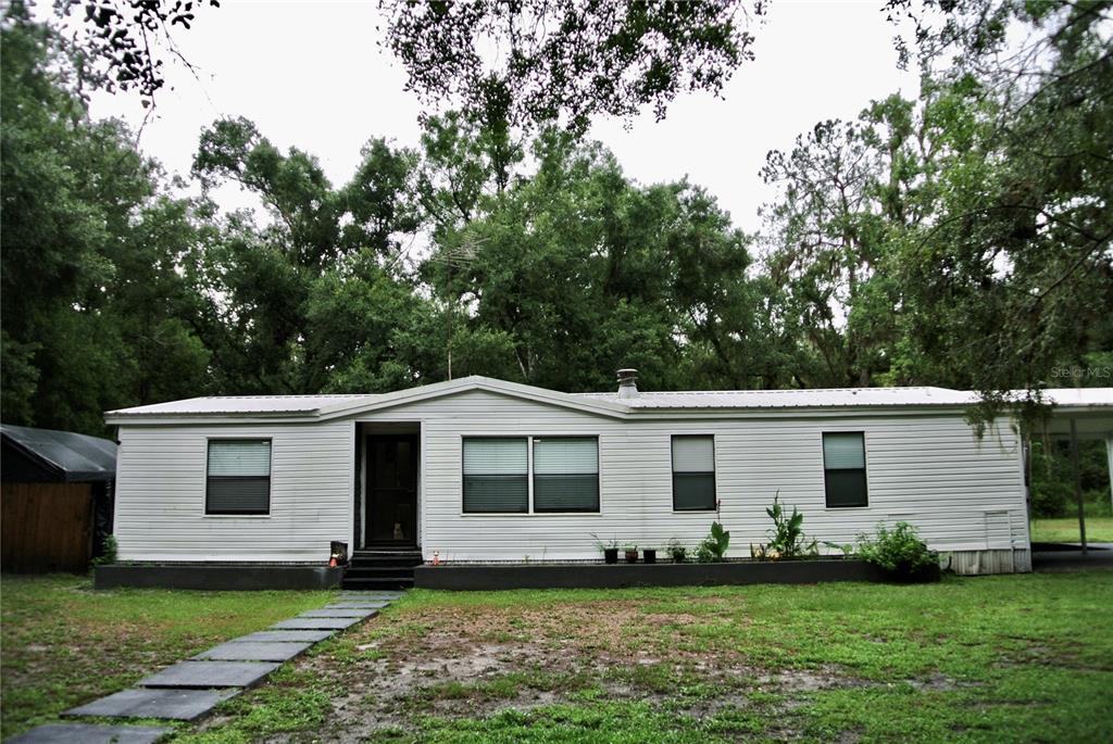 A single-story white mobile home with a metal roof sits on a grassy lot — 38122 CENTRAL AVENUE, ZEPHYRHILLS, FL