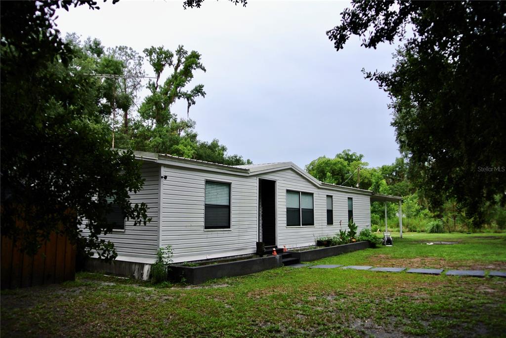 A white single-wide mobile home with a dark foundation sits on a grassy lot — 38122 CENTRAL AVENUE, ZEPHYRHILLS, FL