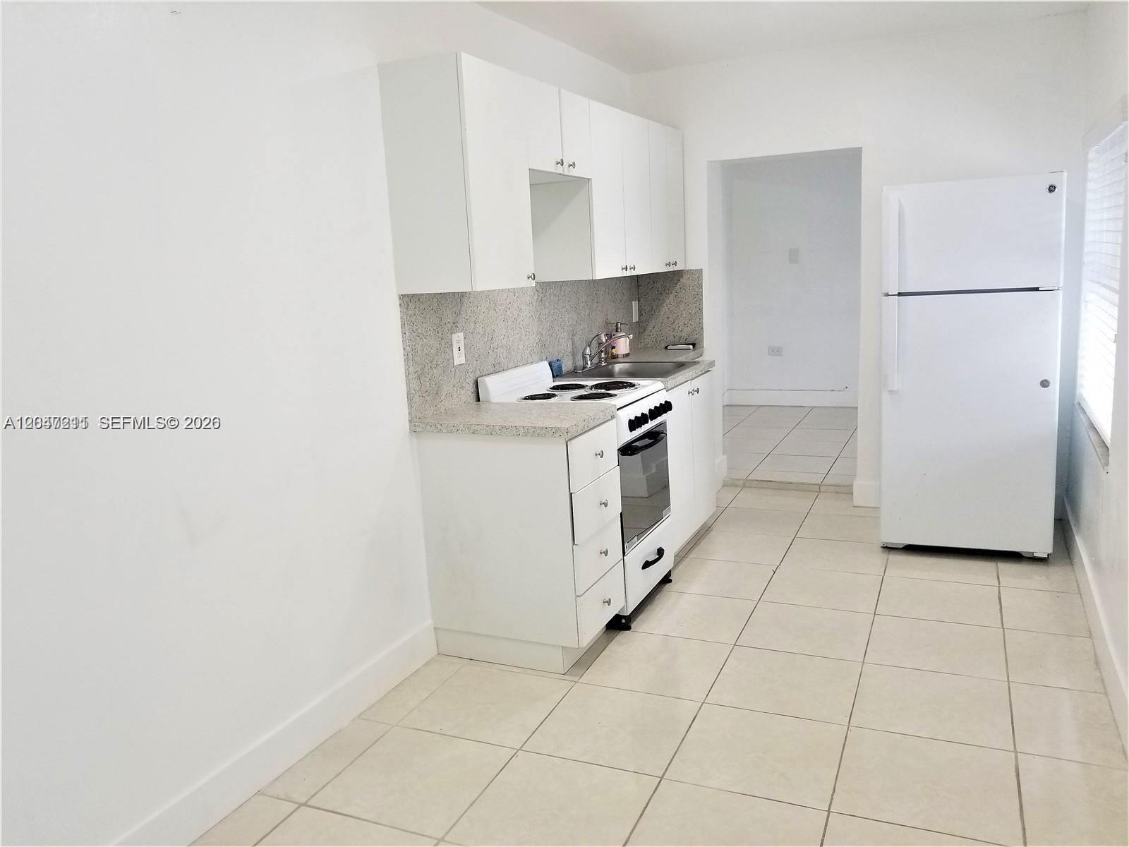 A small kitchen features white cabinets, a white stove, a refrigerator, and light-colored tile flooring — 1829 NW 4th St # 2, Miami FL 33125, MIAMI, FL