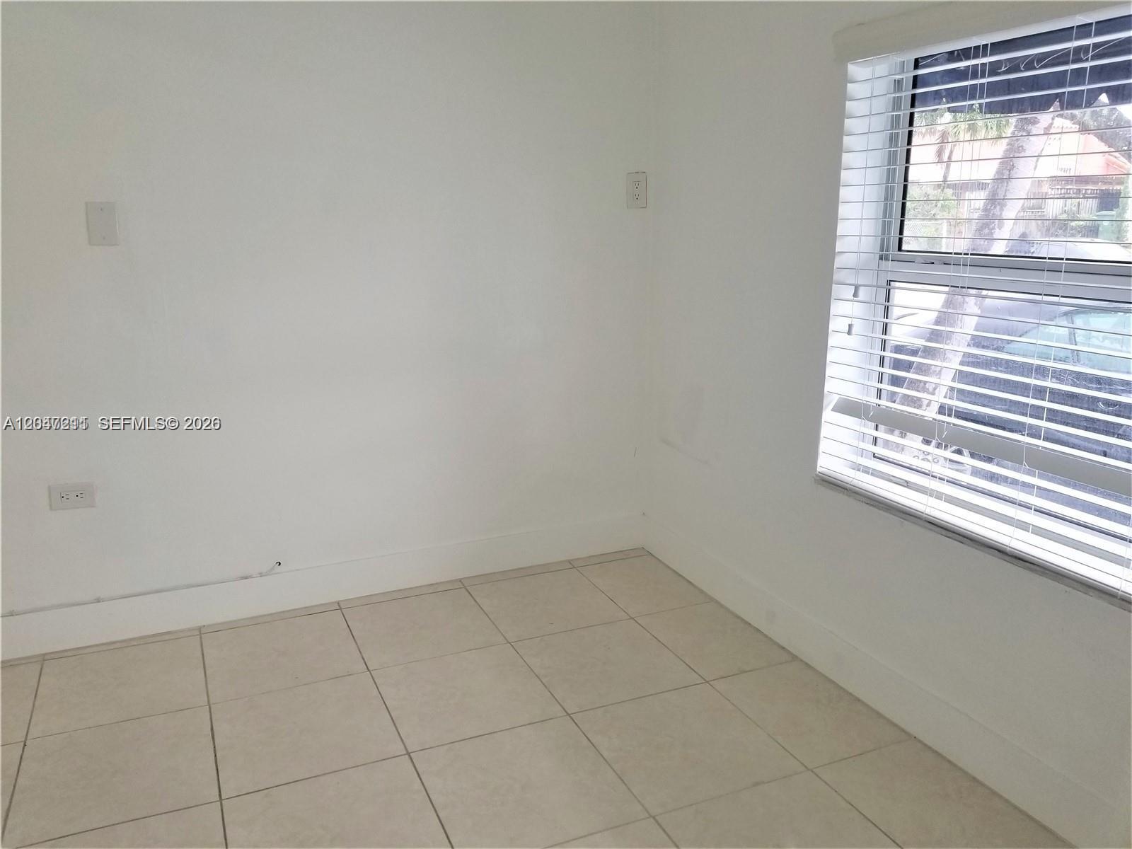 A small, empty room features white walls, light-colored tile flooring, and a window with blinds — 1829 NW 4th St # 2, Miami FL 33125, MIAMI, FL
