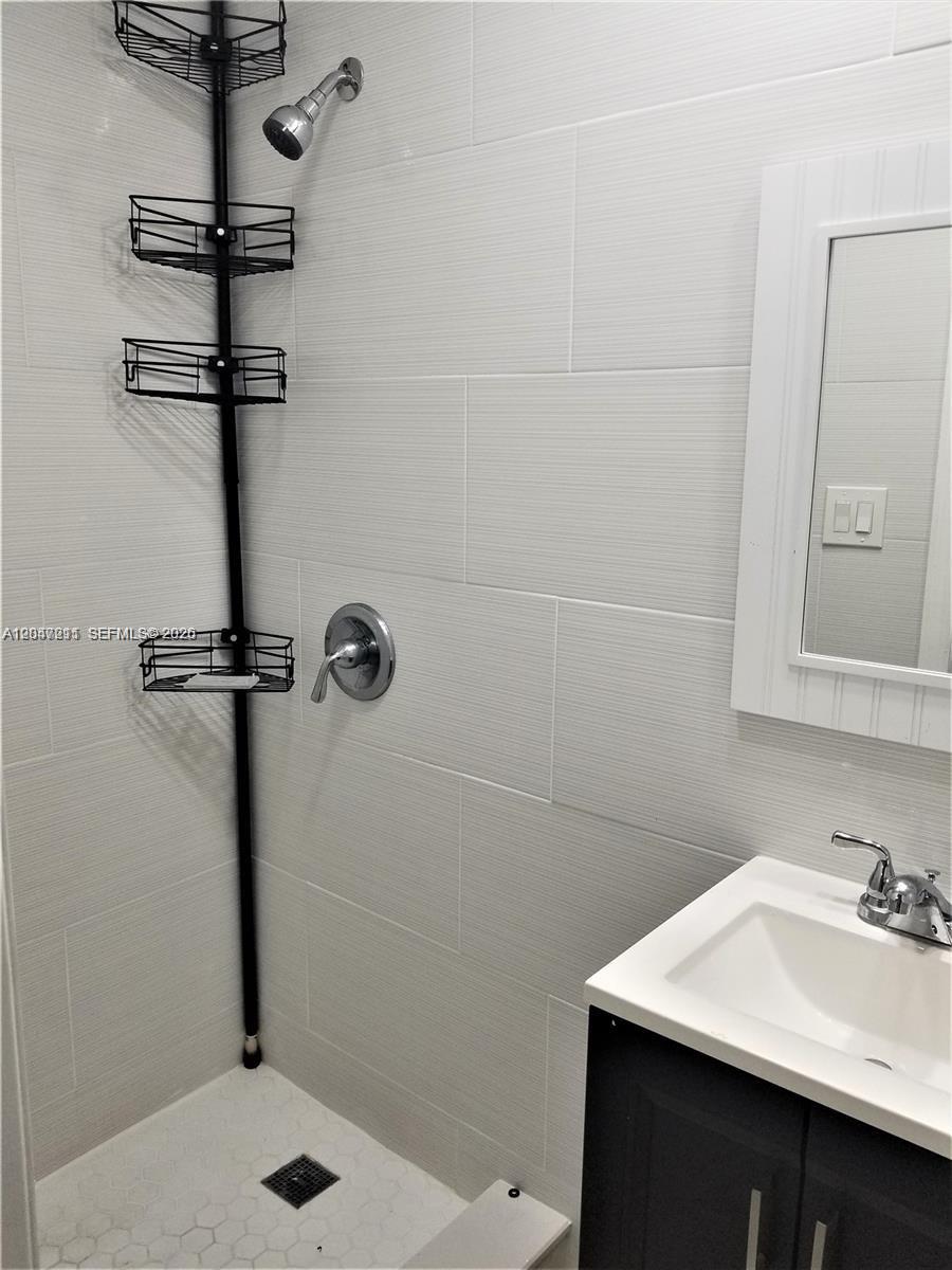 A tiled shower stall features a black tension-pole caddy and a white vanity sink — 1829 NW 4th St # 2, Miami FL 33125, MIAMI, FL