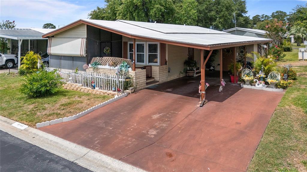 A single-story manufactured home features a covered carport, a small front yard, and white fencing — 3145 GREAT OAK STREET, WESLEY CHAPEL, FL