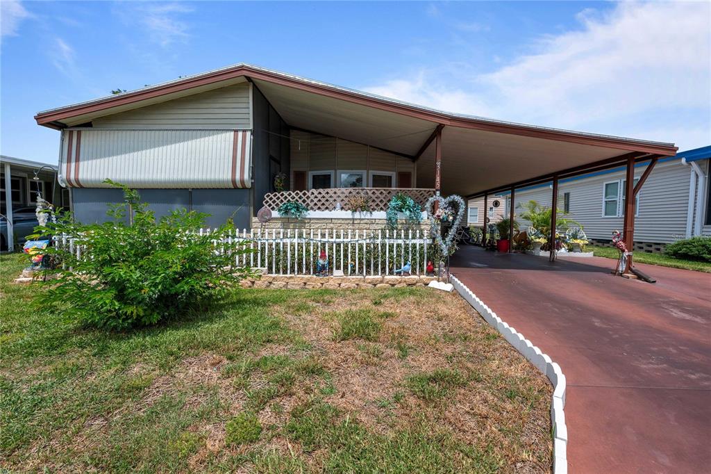 A single-story mobile home features a covered carport, a small front yard, and a white fence — 3145 GREAT OAK STREET, WESLEY CHAPEL, FL