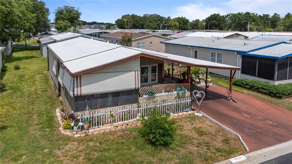 An elevated view of a mobile home with a carport, screened porch, and white fence — 3145 GREAT OAK STREET, WESLEY CHAPEL, FL