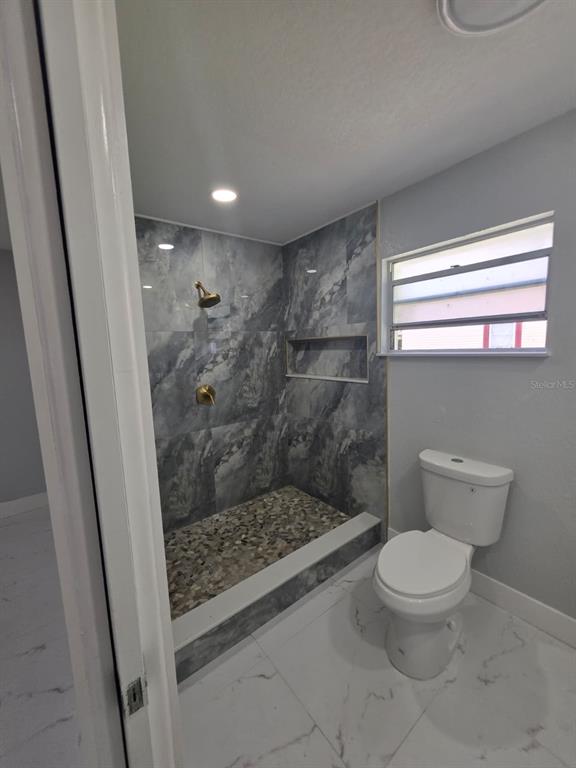 A bathroom features a walk-in shower with gray marble-look tile, a pebble floor, and a toilet — 2428 SW 18TH COURT, OKEECHOBEE, FL