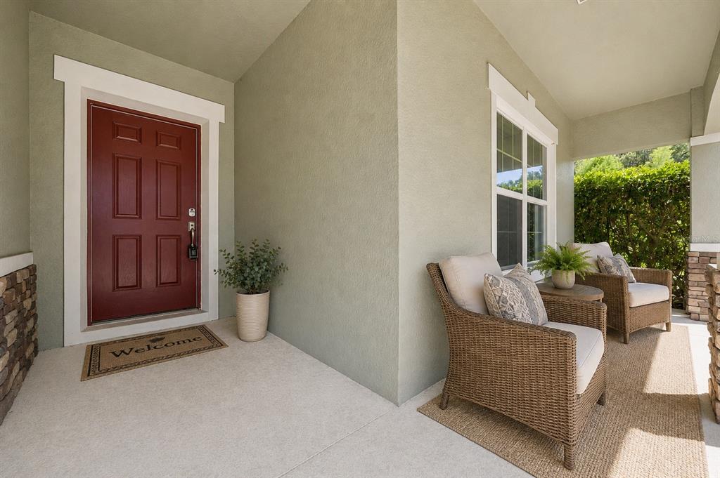 A covered front porch features a red door, two wicker chairs, and a welcome mat — 921 BENDING OAK TRAIL, WINTER GARDEN, FL