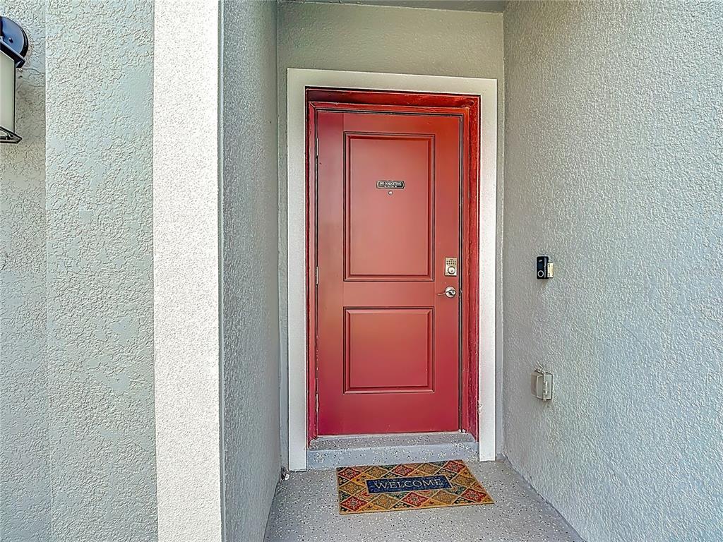 A red front door with a welcome mat sits in a recessed entryway — 550 SEA TURTLE LANE, HAINES CITY, FL