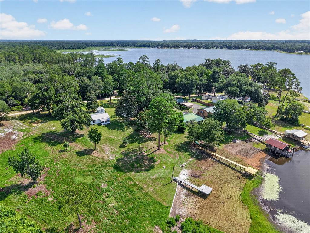 An aerial view shows a grassy property with two houses, trees, and two docks on a lake — 148 LAKE SHORE TERRACE, INTERLACHEN, FL