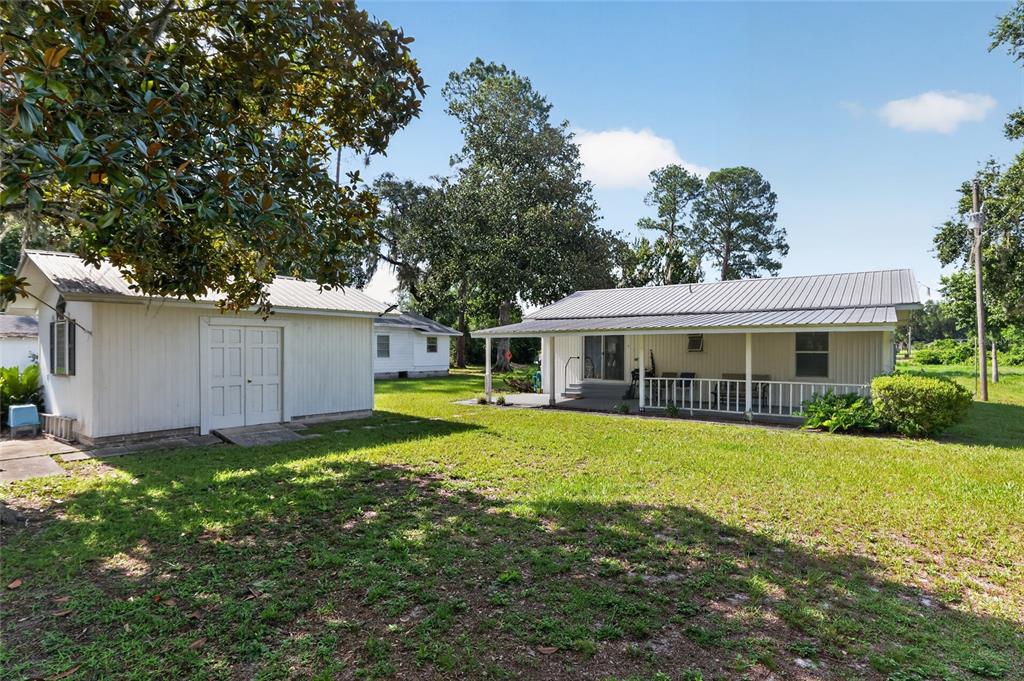 A white detached garage and a house with a covered porch sit on a lawn — 148 LAKE SHORE TERRACE, INTERLACHEN, FL