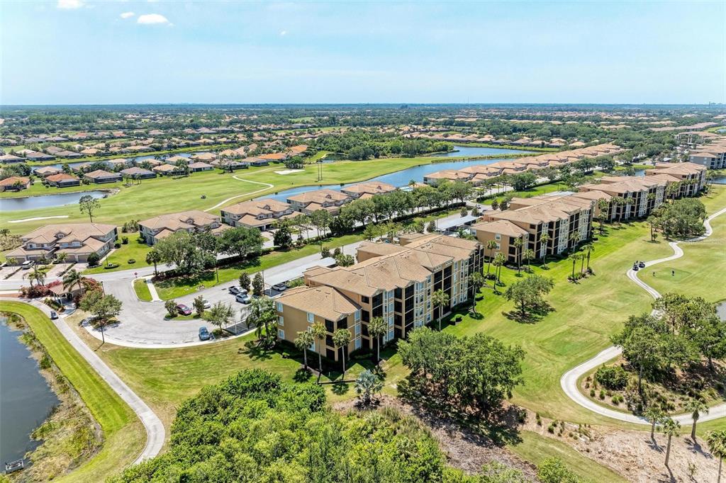 An aerial view shows multi-story apartment buildings surrounded by a golf course and water features — 8403 GRAND ESTUARY TRAIL UNIT 107, BRADENTON, FL