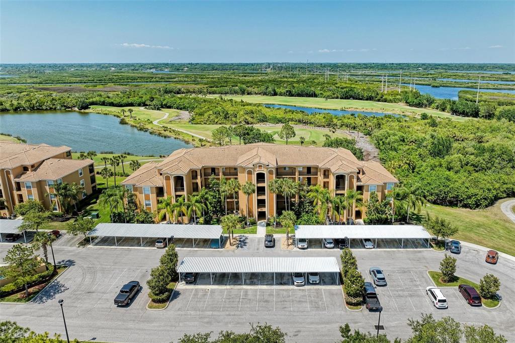 An aerial view of a multi-story apartment building with covered parking and surrounding landscape — 8403 GRAND ESTUARY TRAIL UNIT 107, BRADENTON, FL