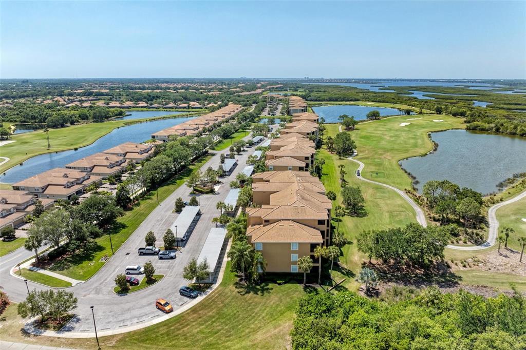 An aerial view shows multi-story residential buildings surrounded by a golf course and water features — 8403 GRAND ESTUARY TRAIL UNIT 107, BRADENTON, FL