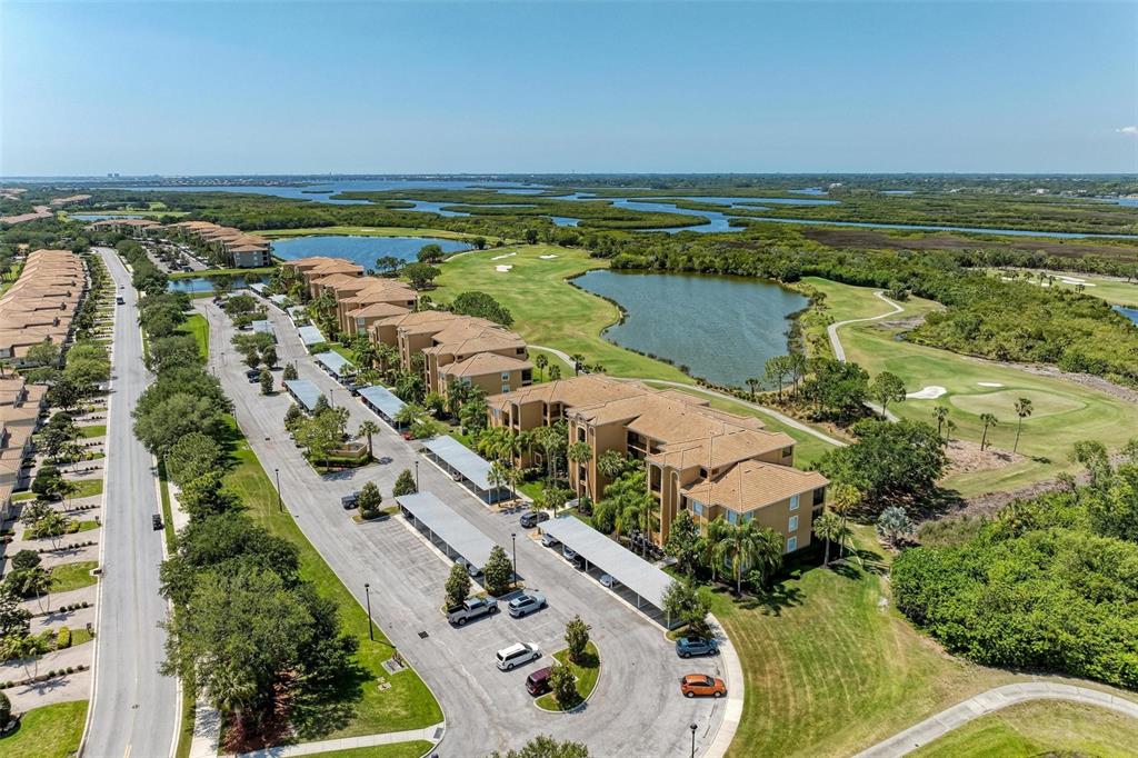 An aerial view shows multi-story apartment buildings, parking lots with carports, and a golf course — 8403 GRAND ESTUARY TRAIL UNIT 107, BRADENTON, FL