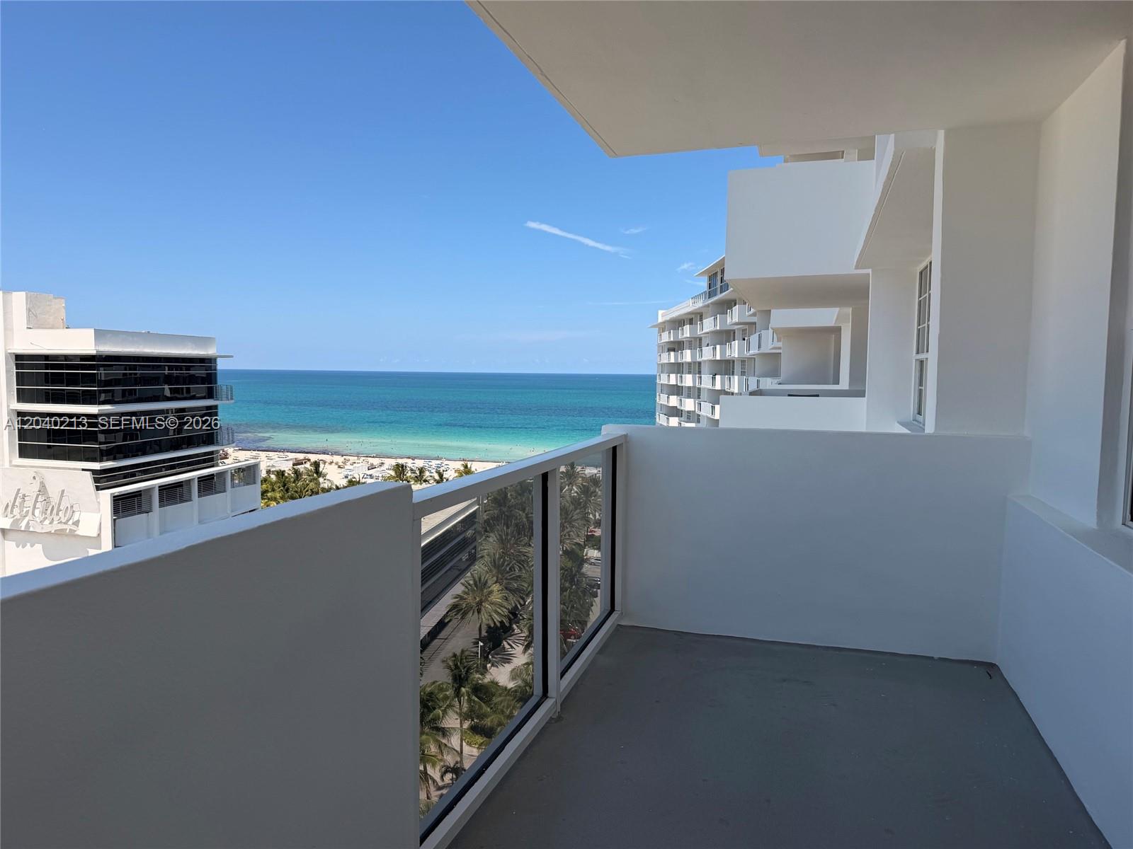 A balcony with a glass railing overlooks the ocean and a nearby white building — 100 Lincoln Rd # 1410, Miami Beach FL 33139, MIAMI BEACH, FL