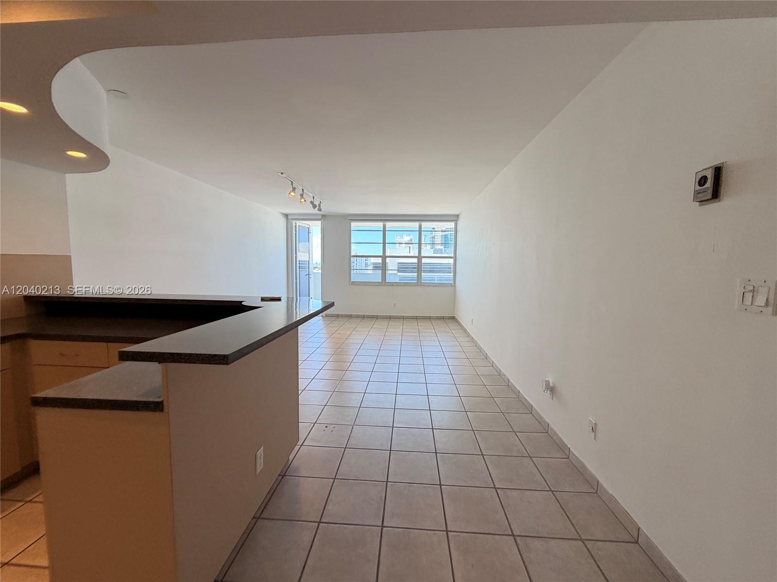 An empty living area features tile flooring, a kitchen counter, and a large window — 100 Lincoln Rd # 1410, Miami Beach FL 33139, MIAMI BEACH, FL