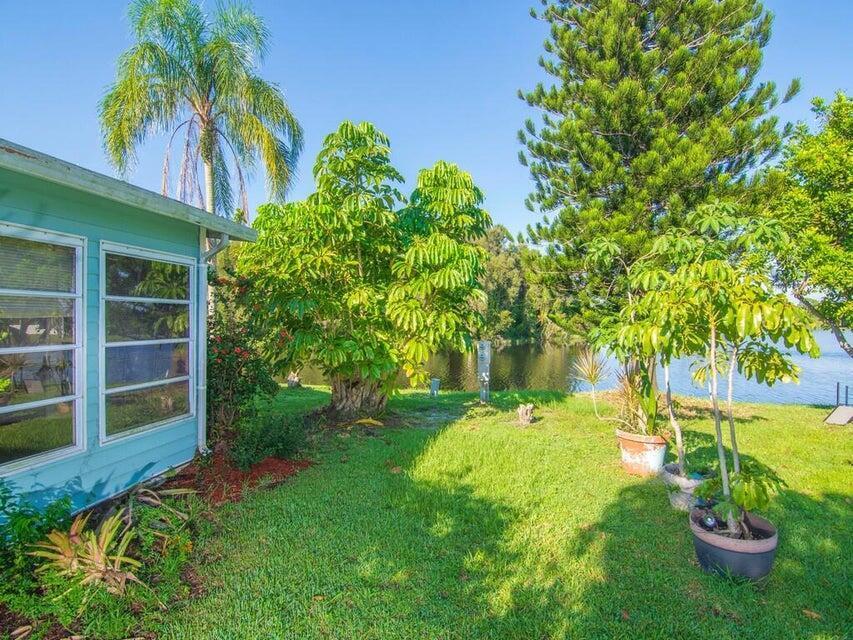 A teal house exterior overlooks a grassy lawn, potted plants, and a lake — 6910 SE Morningside Drive, Stuart FL 34997, STUART, FL