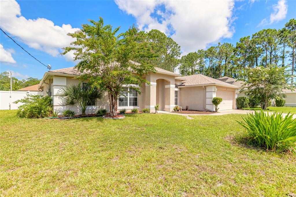 A single-story beige house with a two-car garage, a front lawn, and mature trees — 26 EDGELY LANE, PALM COAST, FL