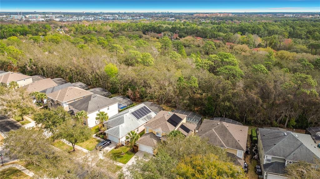 An aerial view shows a suburban neighborhood with houses featuring solar panels and screened pools — 8458 SECRET KEY COVE, KISSIMMEE, FL