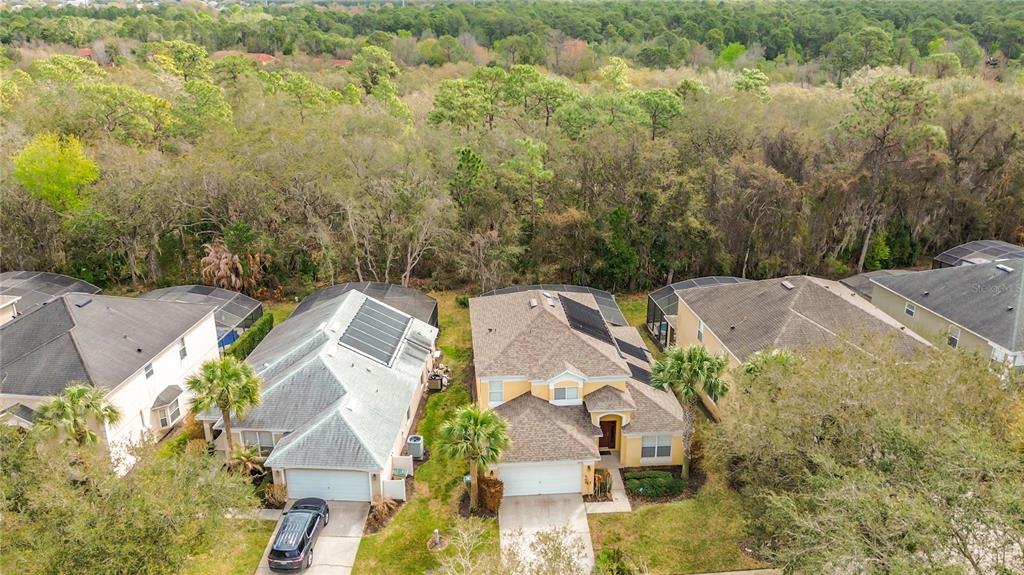 An aerial view shows two suburban houses with solar panels on their roofs near woods — 8458 SECRET KEY COVE, KISSIMMEE, FL