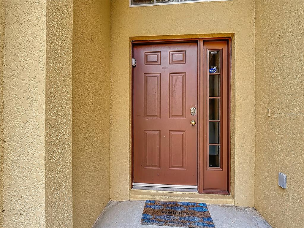 A brown front door with a side window sits in a stucco entryway — 8458 SECRET KEY COVE, KISSIMMEE, FL