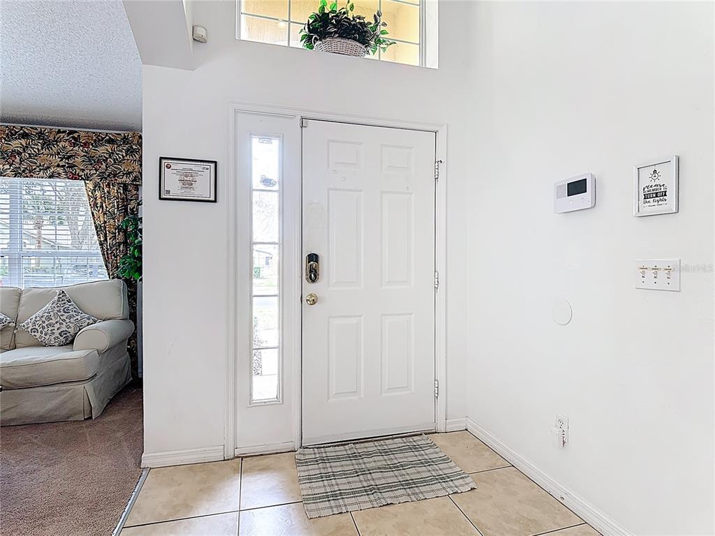 An entryway features a white front door with a sidelight, tile flooring, and a wall-mounted thermostat — 8458 SECRET KEY COVE, KISSIMMEE, FL