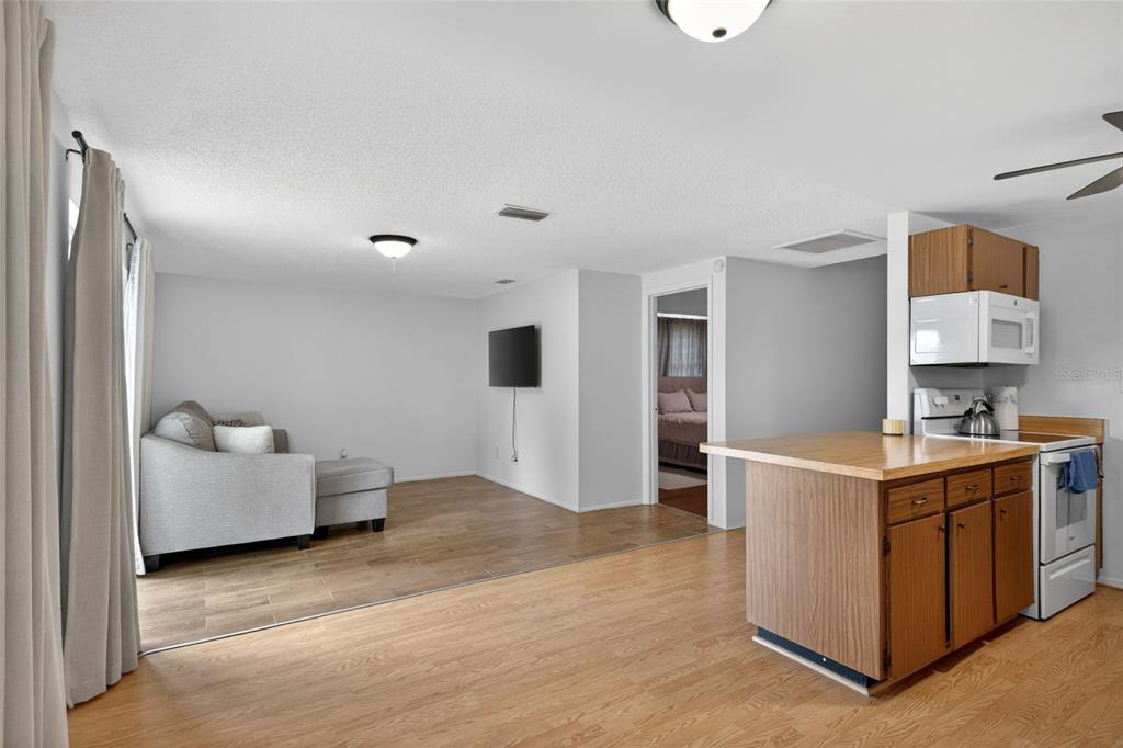A living room with light wood flooring flows into a kitchen with wood cabinets — 6401 REGATTA COURT, TAMPA, FL