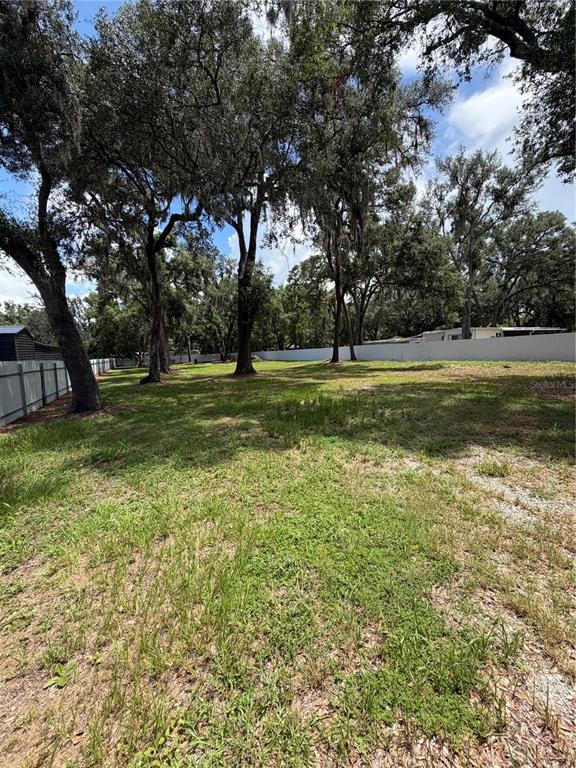 A grassy, vacant lot features several large, mature trees and a white vinyl fence — 11310 BRIGHTRIDGE DRIVE, SEFFNER, FL
