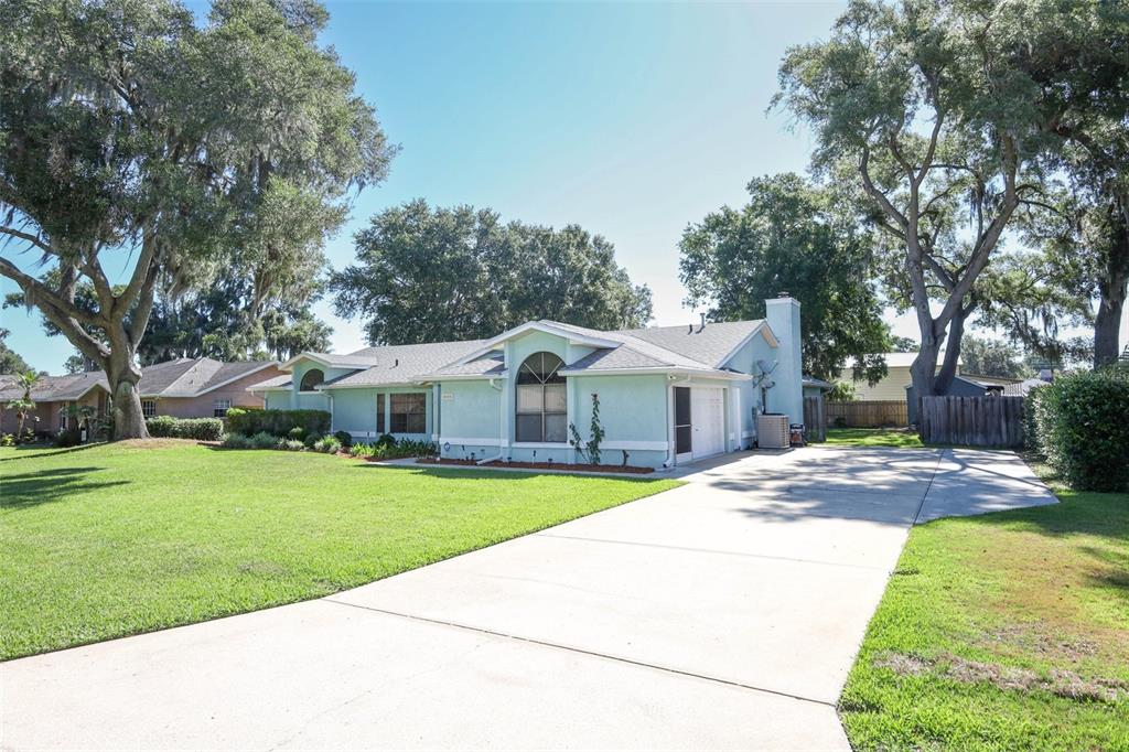 A light blue single-story house with a concrete driveway and large oak trees — 610 YORKTOWN DRIVE, LEESBURG, FL