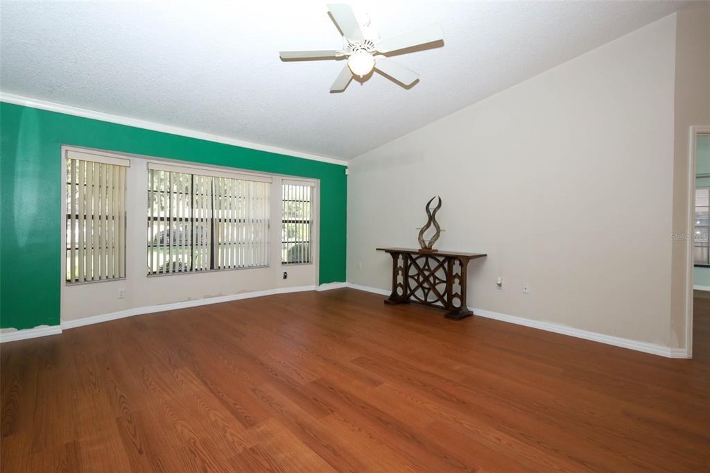 A living room with wood-look flooring, a green accent wall, and a ceiling fan — 610 YORKTOWN DRIVE, LEESBURG, FL