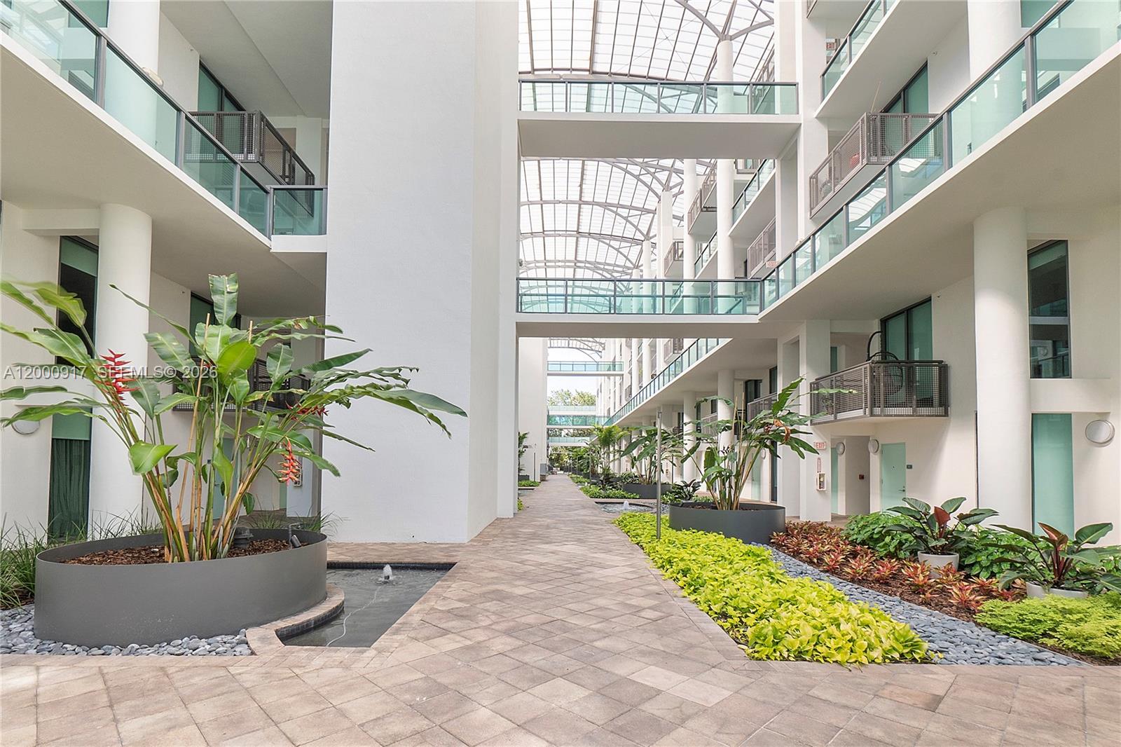 An open-air atrium features a paved walkway, tropical plants, water features, and glass-enclosed walkways — 6000 Collins Ave # 527, Miami Beach FL 33140, MIAMI BEACH, FL