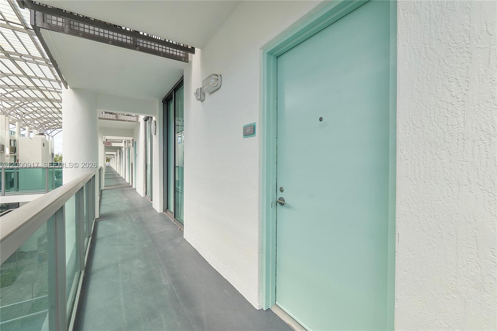 A light blue door leads to a unit along an outdoor apartment building walkway — 6000 Collins Ave # 527, Miami Beach FL 33140, MIAMI BEACH, FL