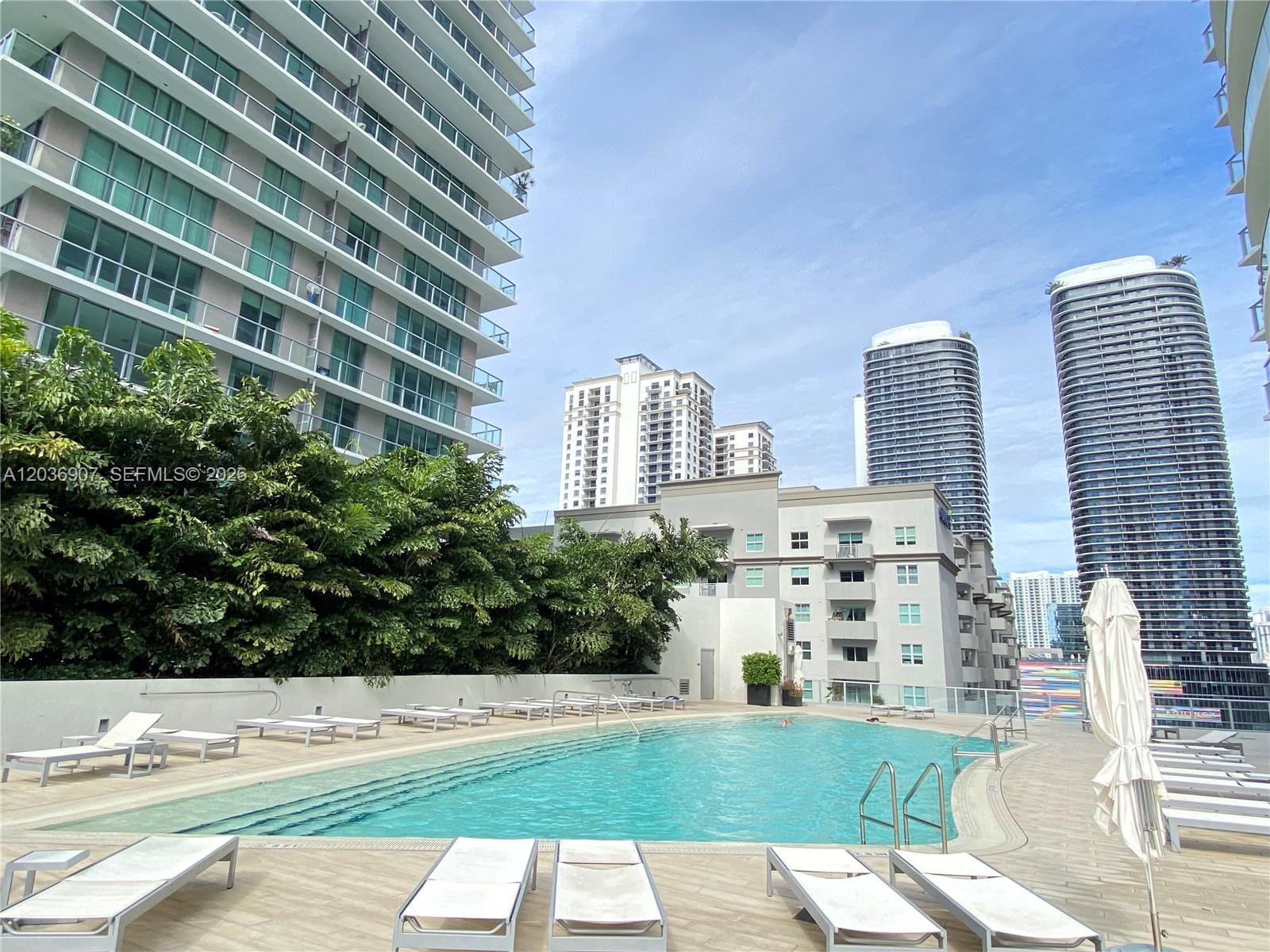 An outdoor swimming pool is surrounded by lounge chairs and tall residential buildings — 1100 S Miami Ave # 1804, Miami FL 33130, MIAMI, FL