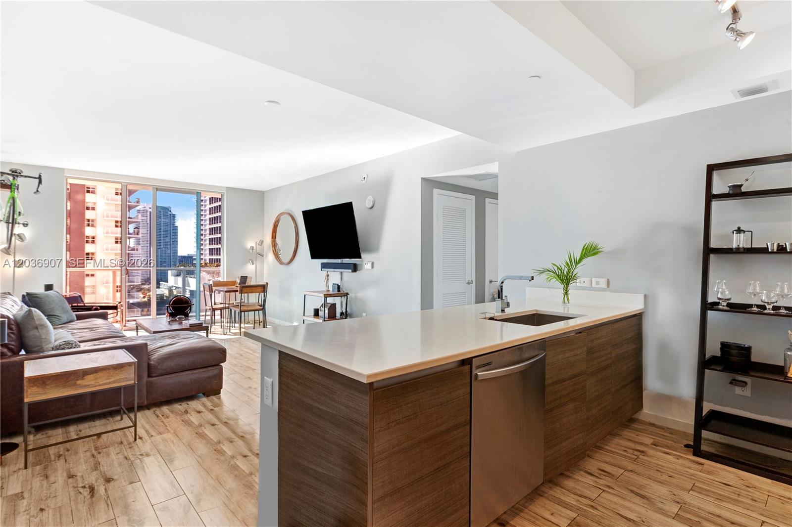 A modern kitchen island with a stainless steel dishwasher overlooks a living room with balcony views — 1100 S Miami Ave # 1804, Miami FL 33130, MIAMI, FL