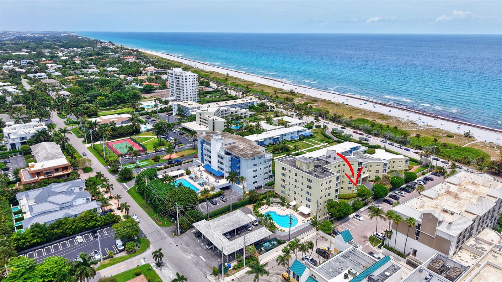 An aerial view shows a multi-story apartment building near a beach with a red arrow — 100 N Ocean Boulevard # 105, Delray Beach FL 33483, DELRAY BEACH, FL