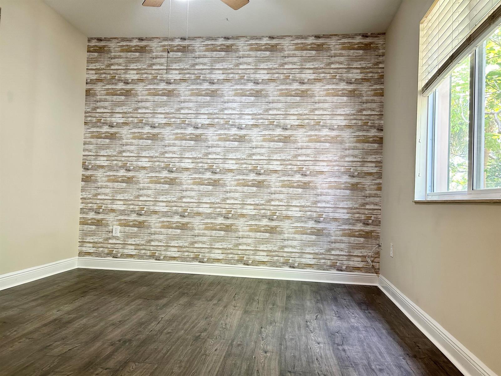 A room with dark wood-look flooring and a feature wall with rustic wood-plank wallpaper — 3803 NW 5th Terrace, Boca Raton FL 33431, BOCA RATON, FL